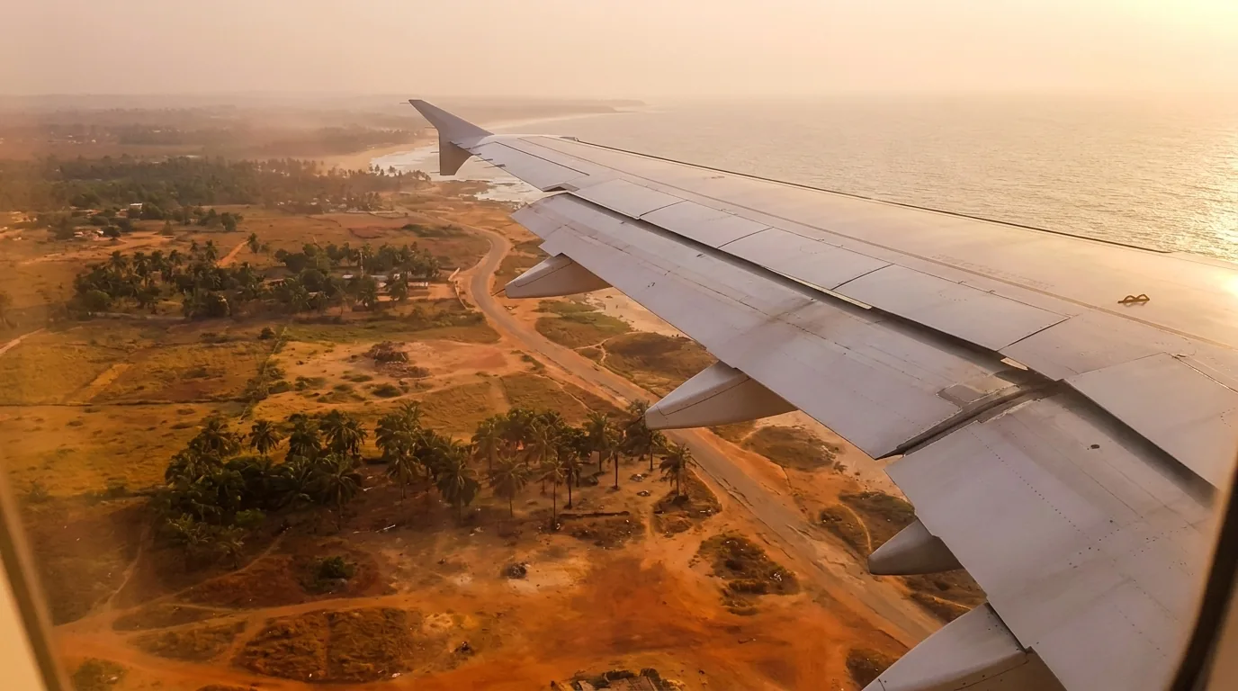 Illustration: an airplane wing over the West African coast at golden hour, descending to land.